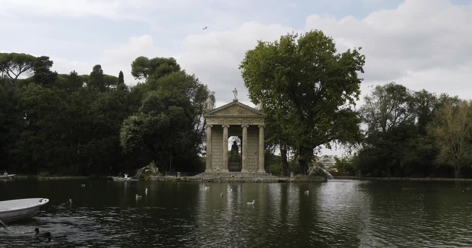 Ducks swim near a rowboat on a lake near a memorial building