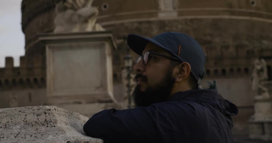 A man stands near stone buildings and statues