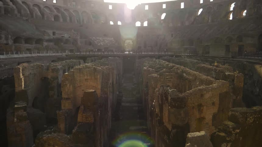 The sun casts light and shadow on the ruins of an ancient colosseum