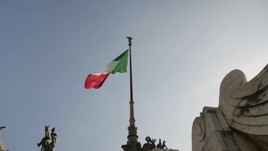 A red, white, and green flag blows in the wind against a blue sky