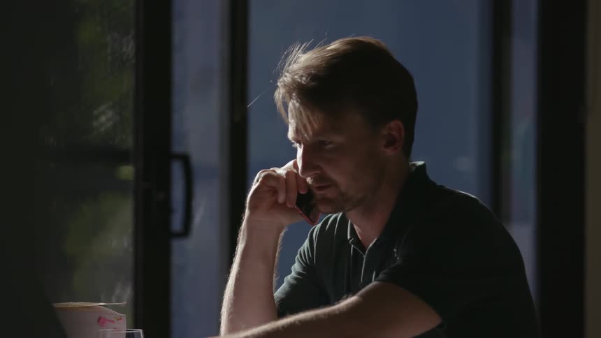 A man answers his phone and types on a laptop