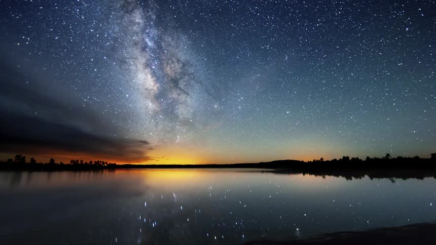 Stars pass over a reflective lake at night