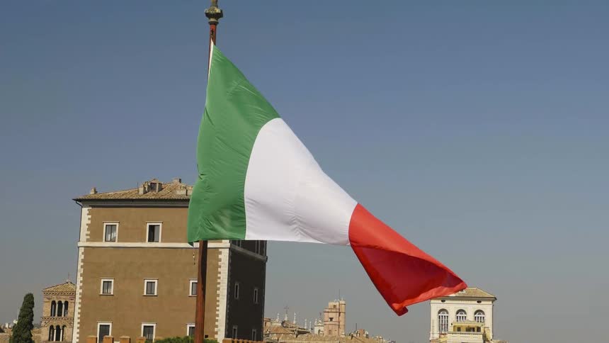A flag blows in the wind with buildings behind it