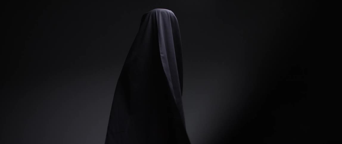 A person covered in a black sheet with a black background