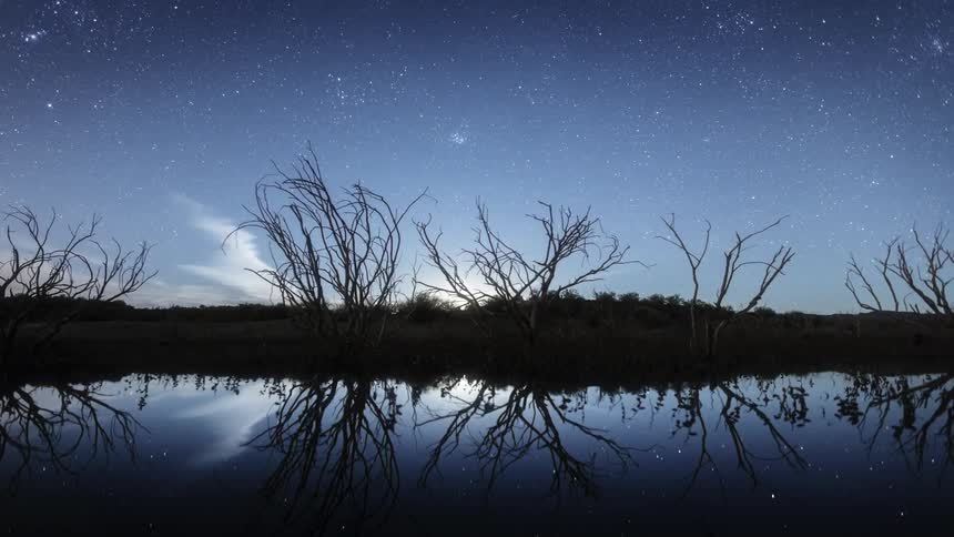 The moon sinking behind a pool of water and trees