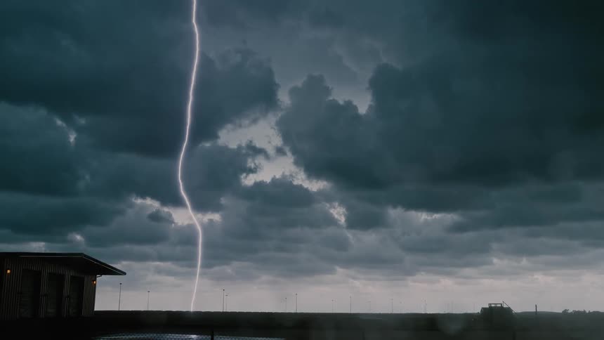 Lightning strikes near a small building on flat land