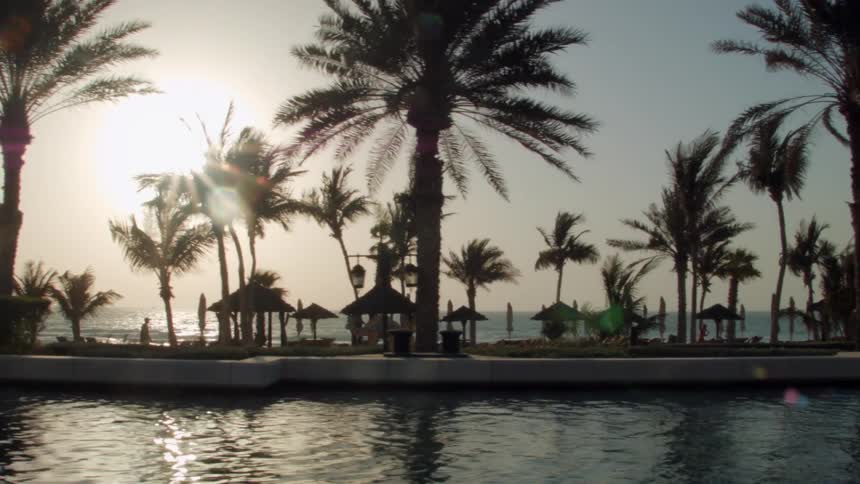 The sun shines through palm trees and beach huts