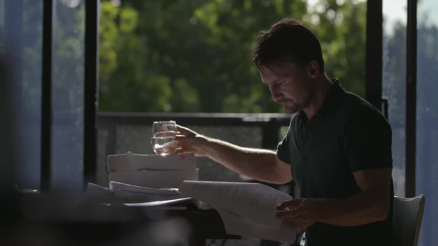 A man takes a drink of water while reading papers