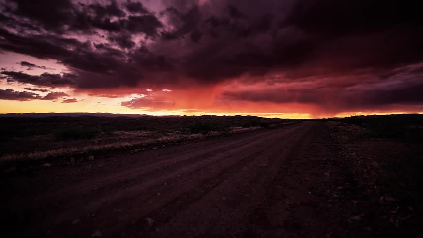 Storm clouds form and move over a dirt road at dusk