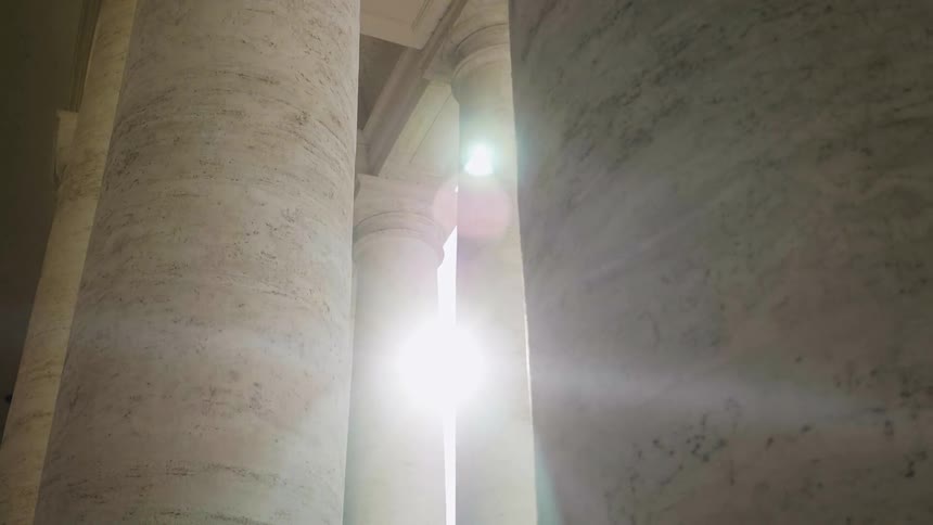 The sun shines between two rows of marble columns
