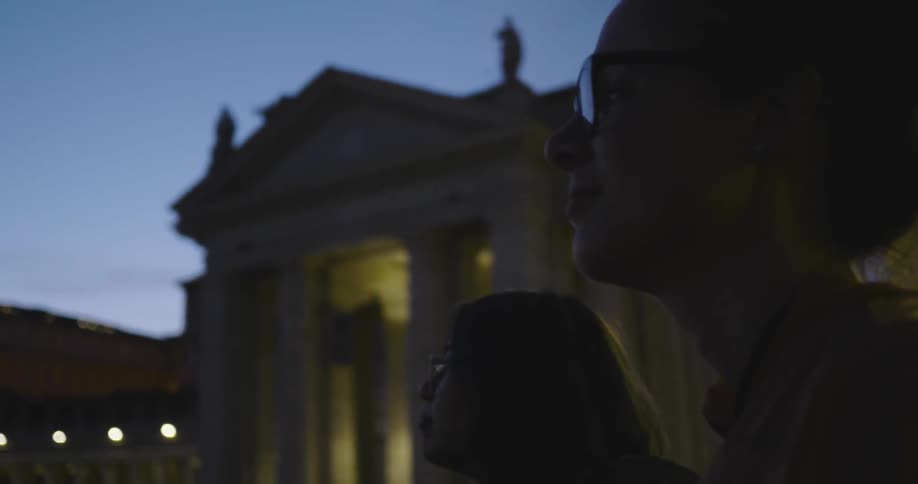 Two women are looking at monuments in a city at dusk