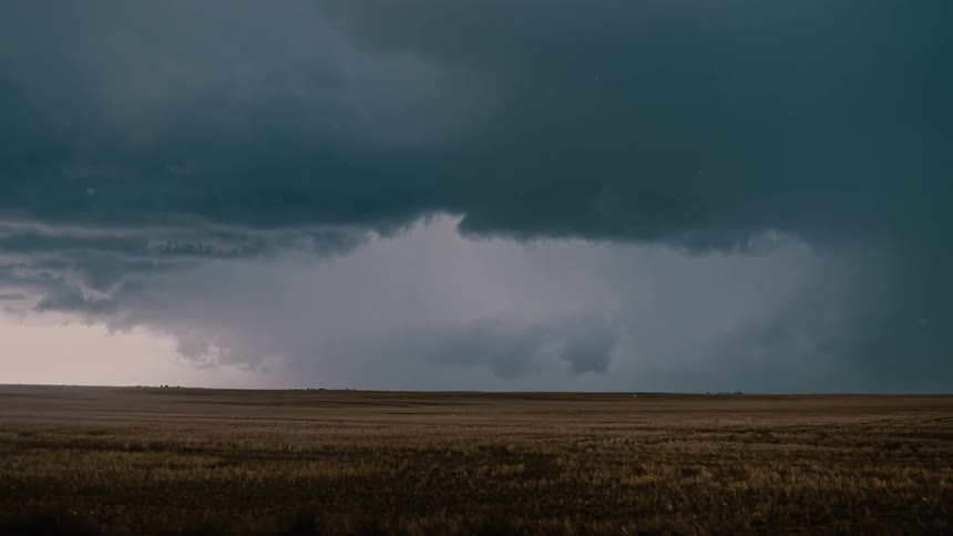 Debris flies through a rural field with storm clouds in the distance