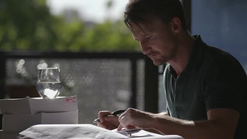 Man sits at a table next to a window reading a paper
