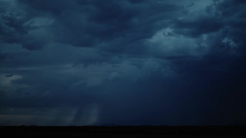 The sky is full of large clouds pouring rain and lighting up the field with lightning