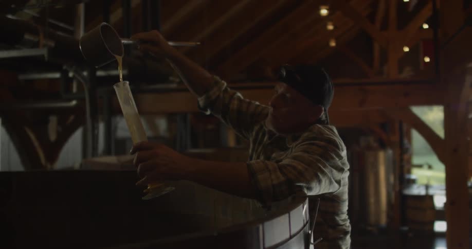A man pours beer into a glass vial leaning over a vat