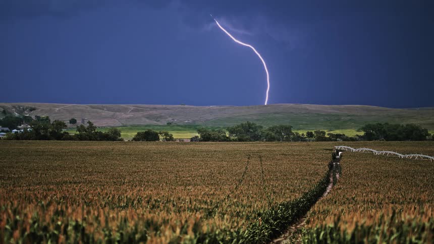 Lightning striking a hill behind a field of crops