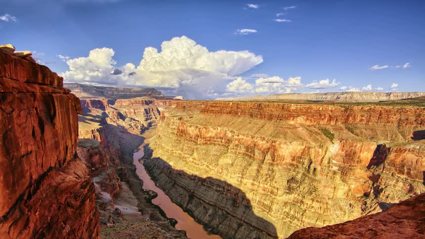 Clouds move across a steep canyon with a river during the day