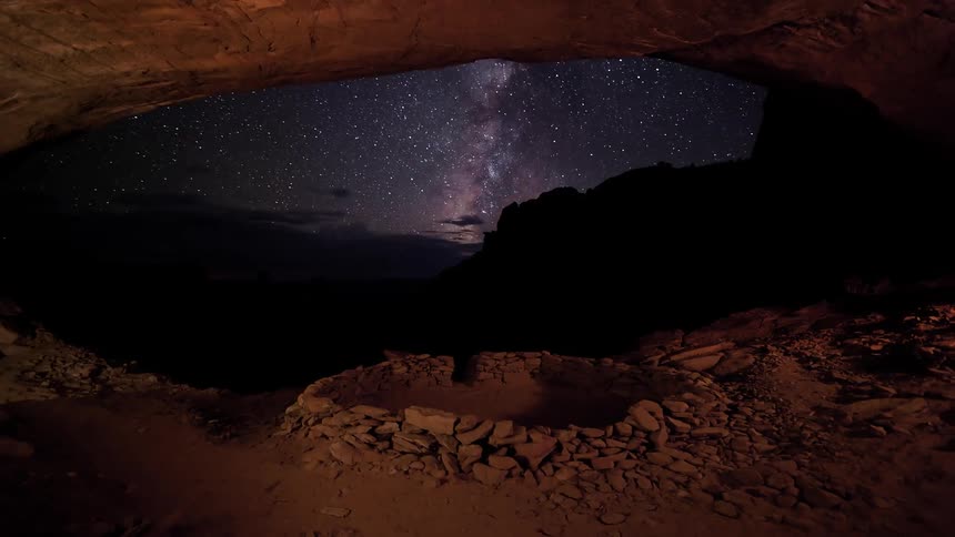 View inside of a cave looking out as lightning flashes and stars shine