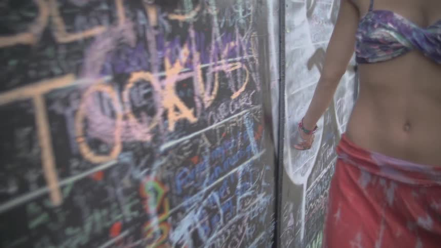 A woman tracing her hand across a graffiti filled wall