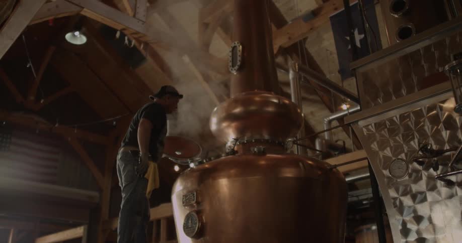 A man opens the door of distillery equipment and steam escapes