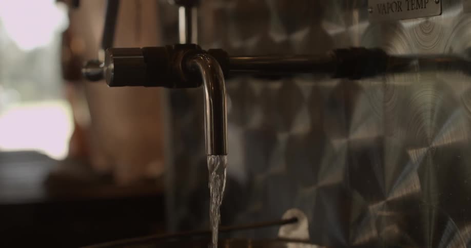 Liquid pours into a metal bucket at a distillery