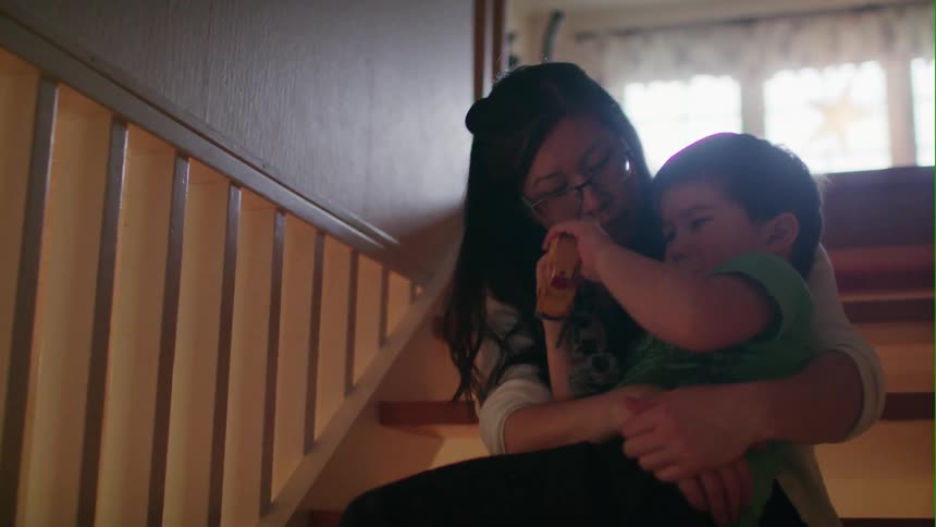 A woman sitting on the stairs holds and hugs a boy