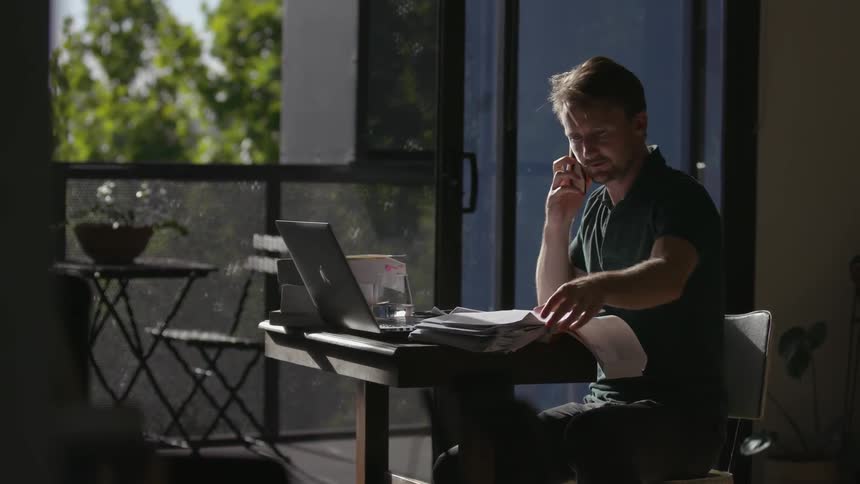 A man is working talking on the phone and looking through papers