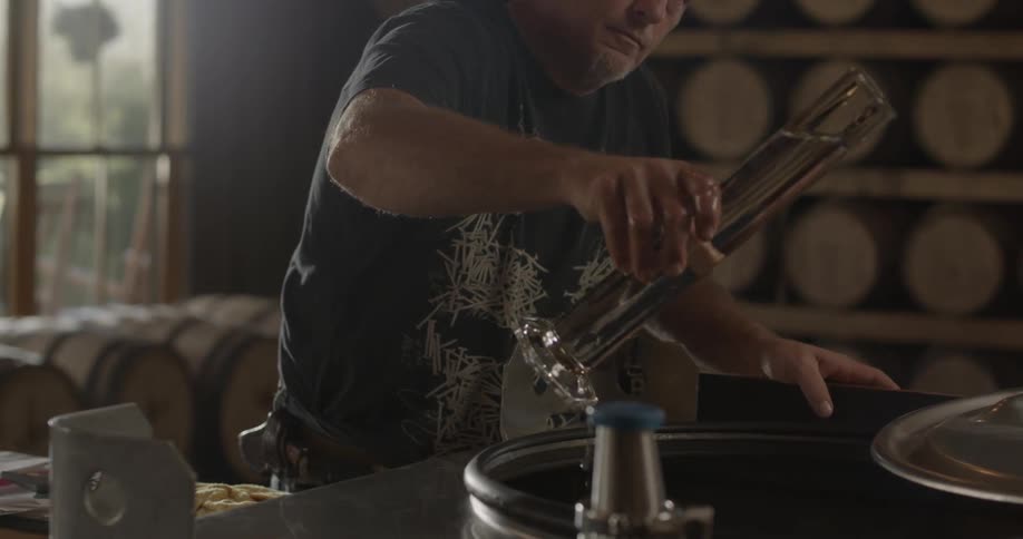 A man fills a tube with liquid from a vat and pours some out