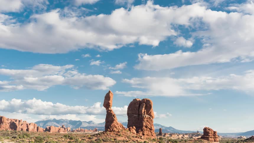 White clouds drift over rock pillars in a desert landscape during the day