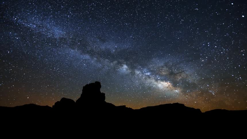 Stars move in the night sky behind a craggy peak