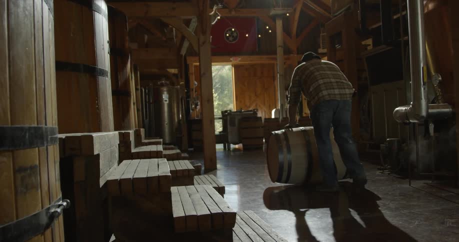 A distillery worker rolls a barrel across the floor