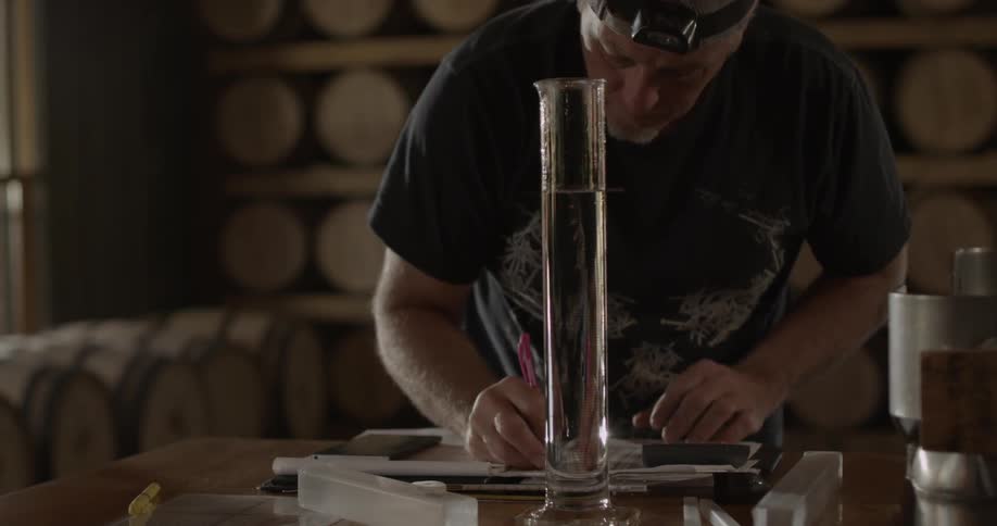 A man standing at a table in front of a glass cylinder is taking notes