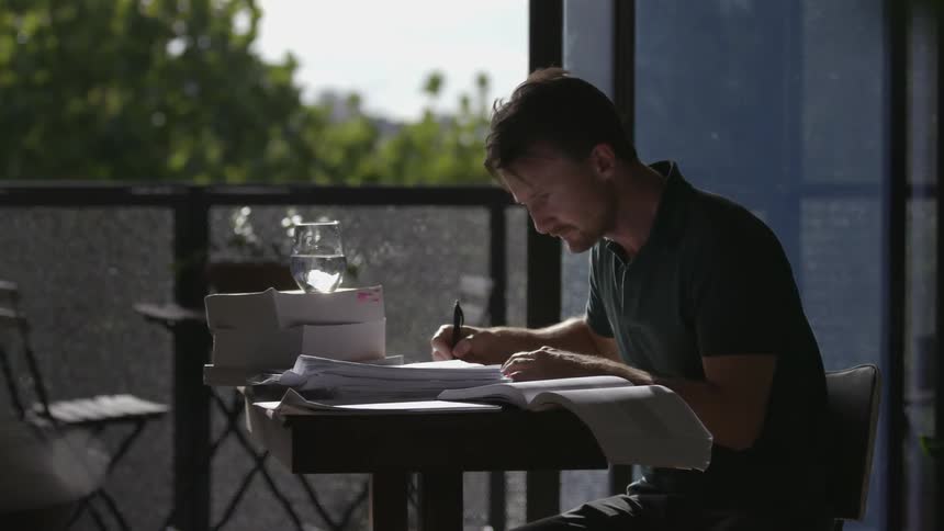 A man works at a small table near an open balcony door
