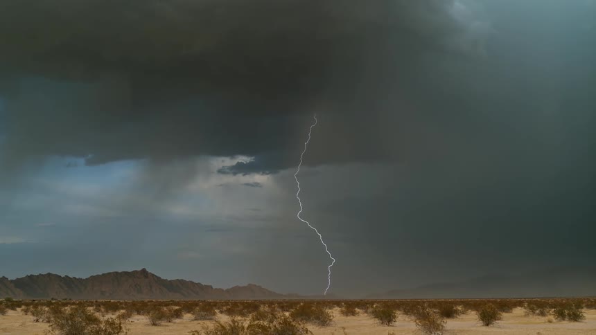 Storm clouds produce lightning and rain as they move across a desert landscape