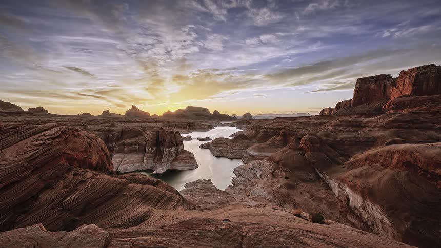 Clouds move overhead as the sun sets on a canyon