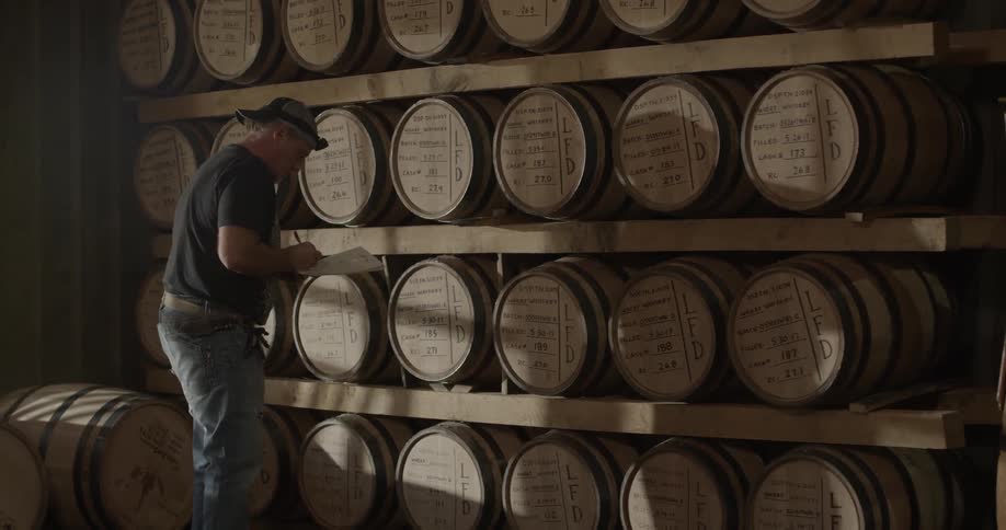 A distillery worker examines barrels of whiskey
