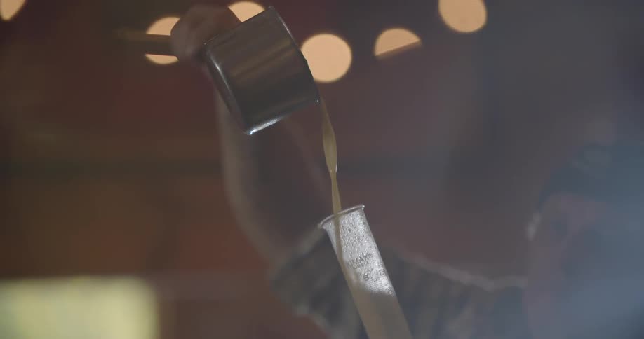 A man pours beer from a pot into a vial