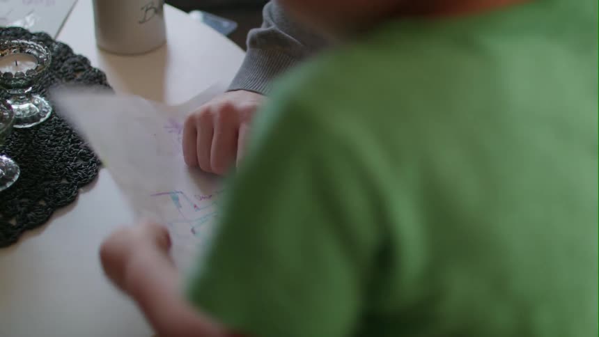 An adult is pointing out something for a child on the child's drawing