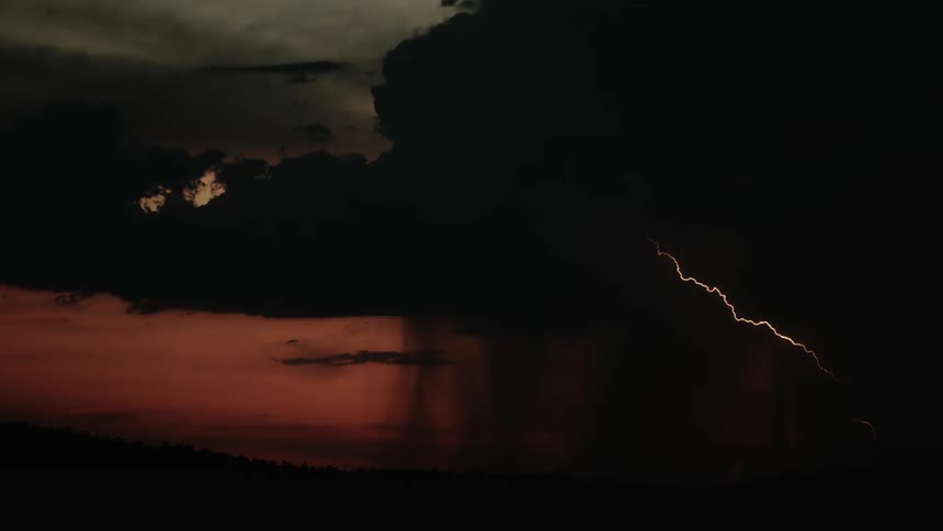 Storm clouds move across the sky trailing rain and lightning