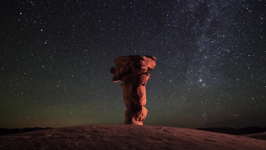 Stars move in the night sky behind a natural rock column