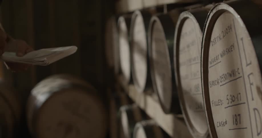 A man is taking notes as he checks barrels lined up on shelves