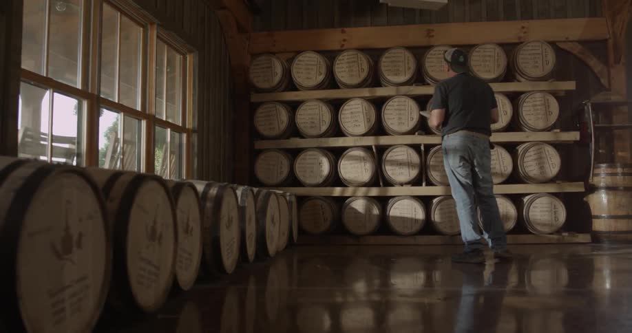 A man is taking notes as he checks barrels lined up on shelves