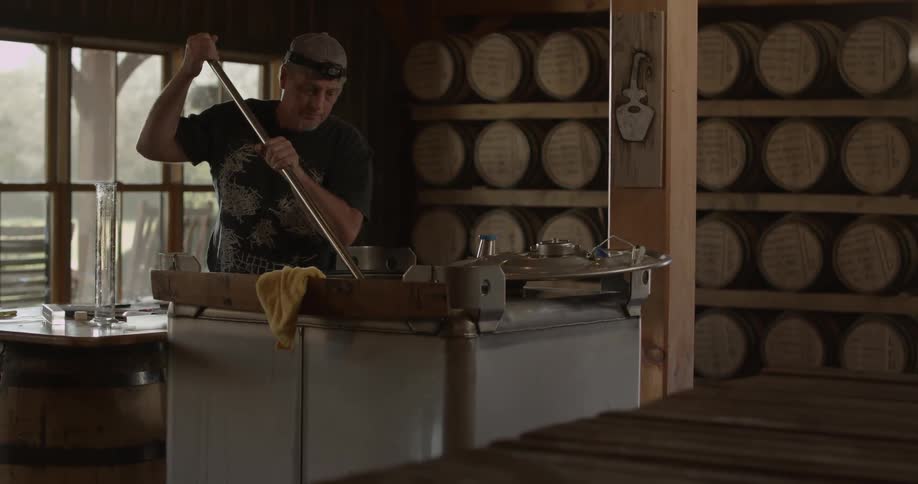 A distillery worker holds a large stirring stick