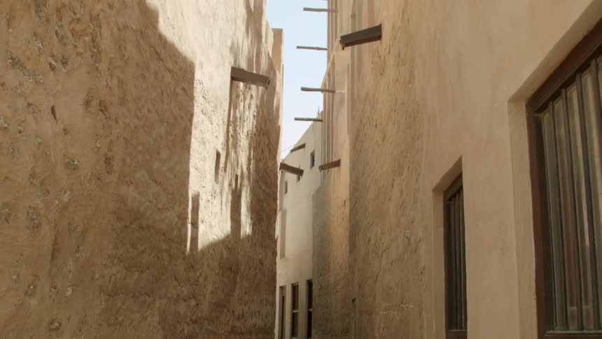 The shadow from a tree plays on the stone walls of a narrow alley