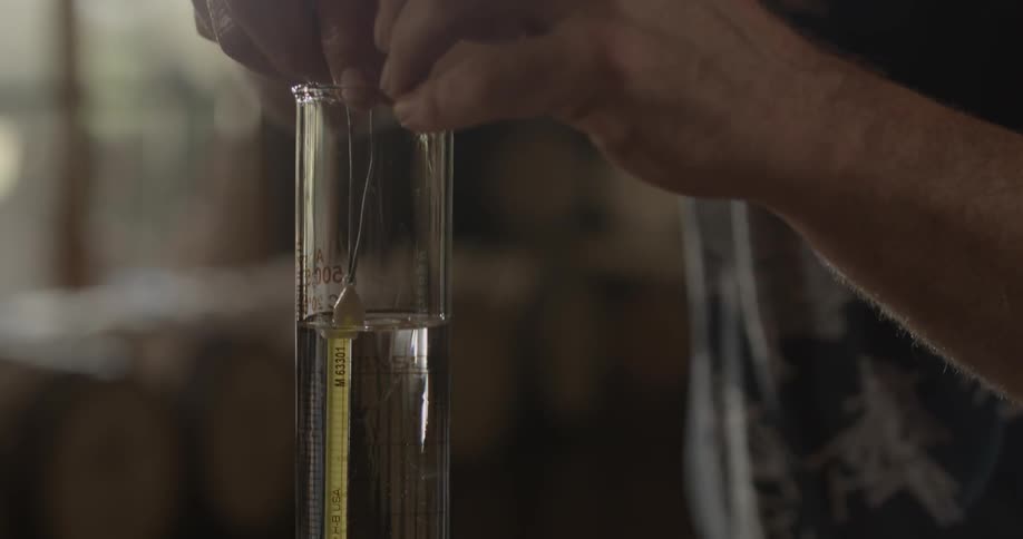 A man lowers a thermometer into a glass cylinder filled with clear liquid