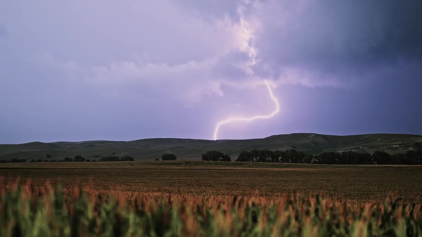 Lightning strikes a hill behind a field of crops