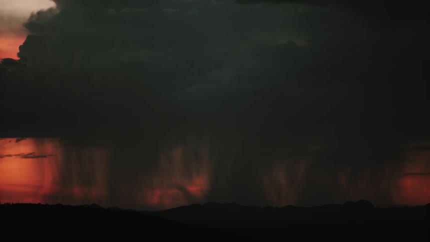 Storm clouds produce lightning and rain as they move across a desert landscape