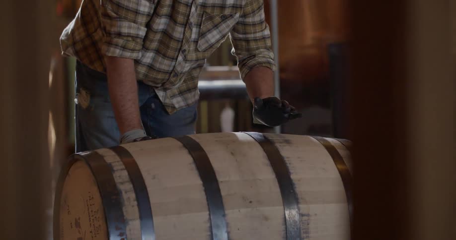 A man rolls a large barrel in a warehouse