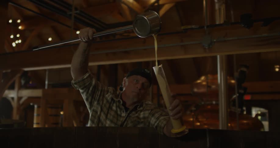A distillery worker pours liquid into a graduated cylinder