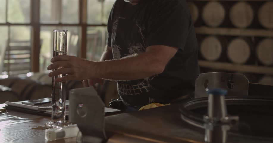 A distillery worker holds a graduated cylinder